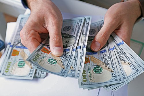 hands holding dozens of hundred dollar bills